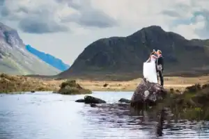 Bride and groom embracing on scenic rock by a lake on the Isle of Skye with a mountain backdrop