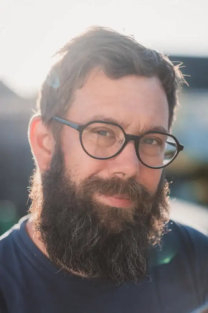 Bearded man with glasses in sunlight smiling at camera