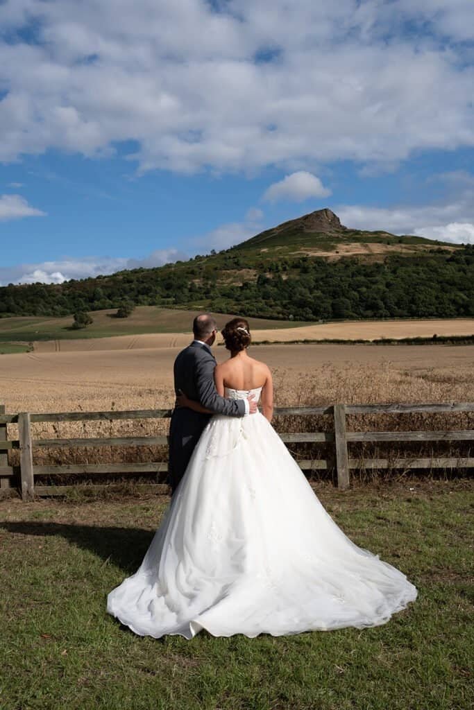 Bride and groom embracing with scenic countryside backdrop at Newton Roseberry