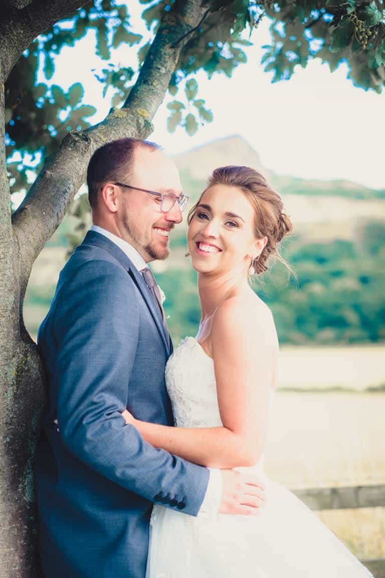 Bride and groom smiling under a tree at outdoor wedding near Roseberry Topping, Newton Roseberry.
