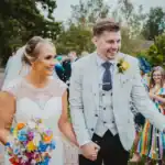 Bride and groom joyfully walk hand in hand down a confetti run in Teesside