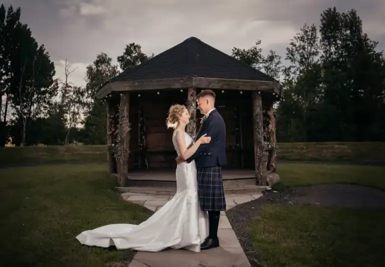 Bride and groom share a romantic moment by a rustic gazebo at Silverwood Resort in Perth, Scotland