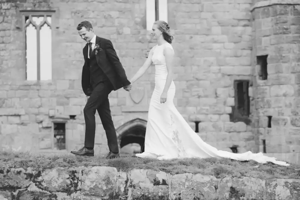 Bride and groom walk hand in hand near an ancient castle in Rothbury, Northumberland