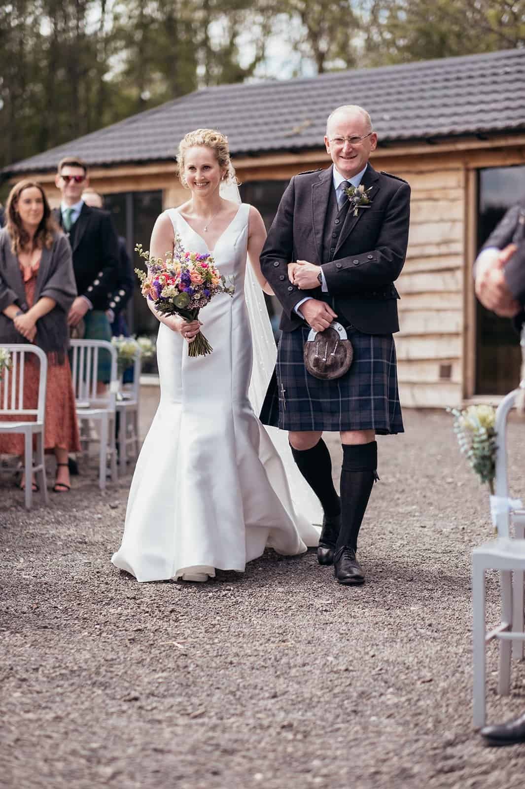 Bride walking down outdoor aisle with her father holding bouquet