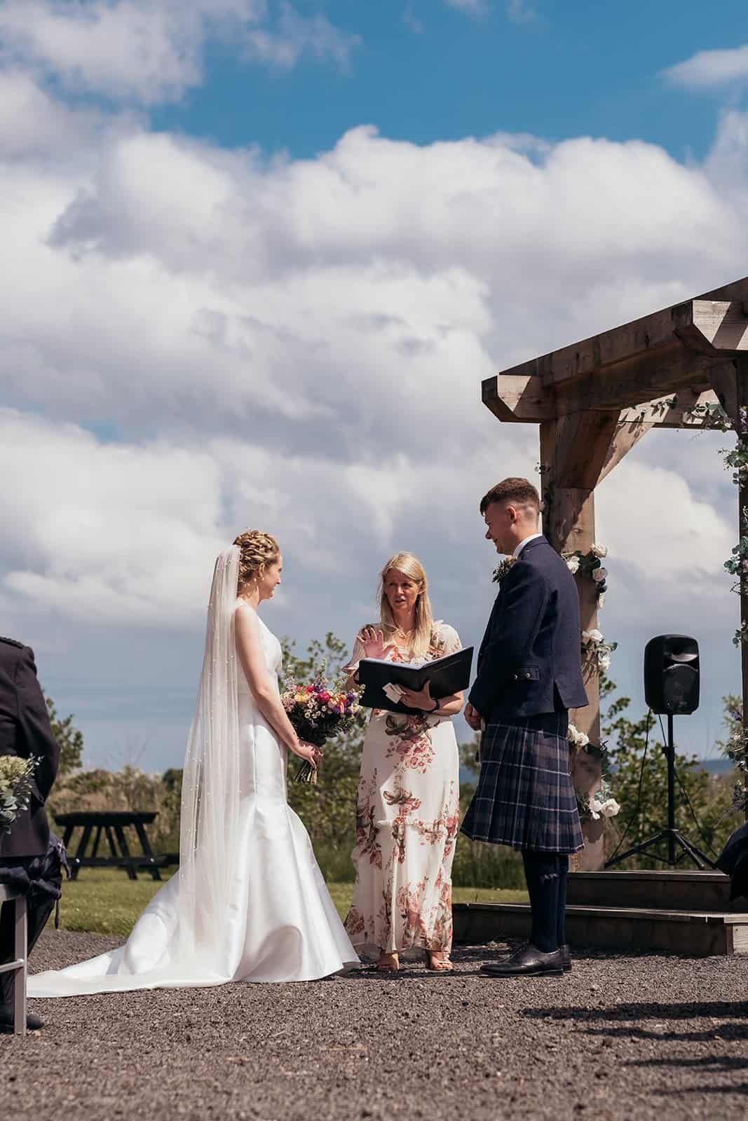 Outdoor wedding ceremony under blue sky with smiling couple