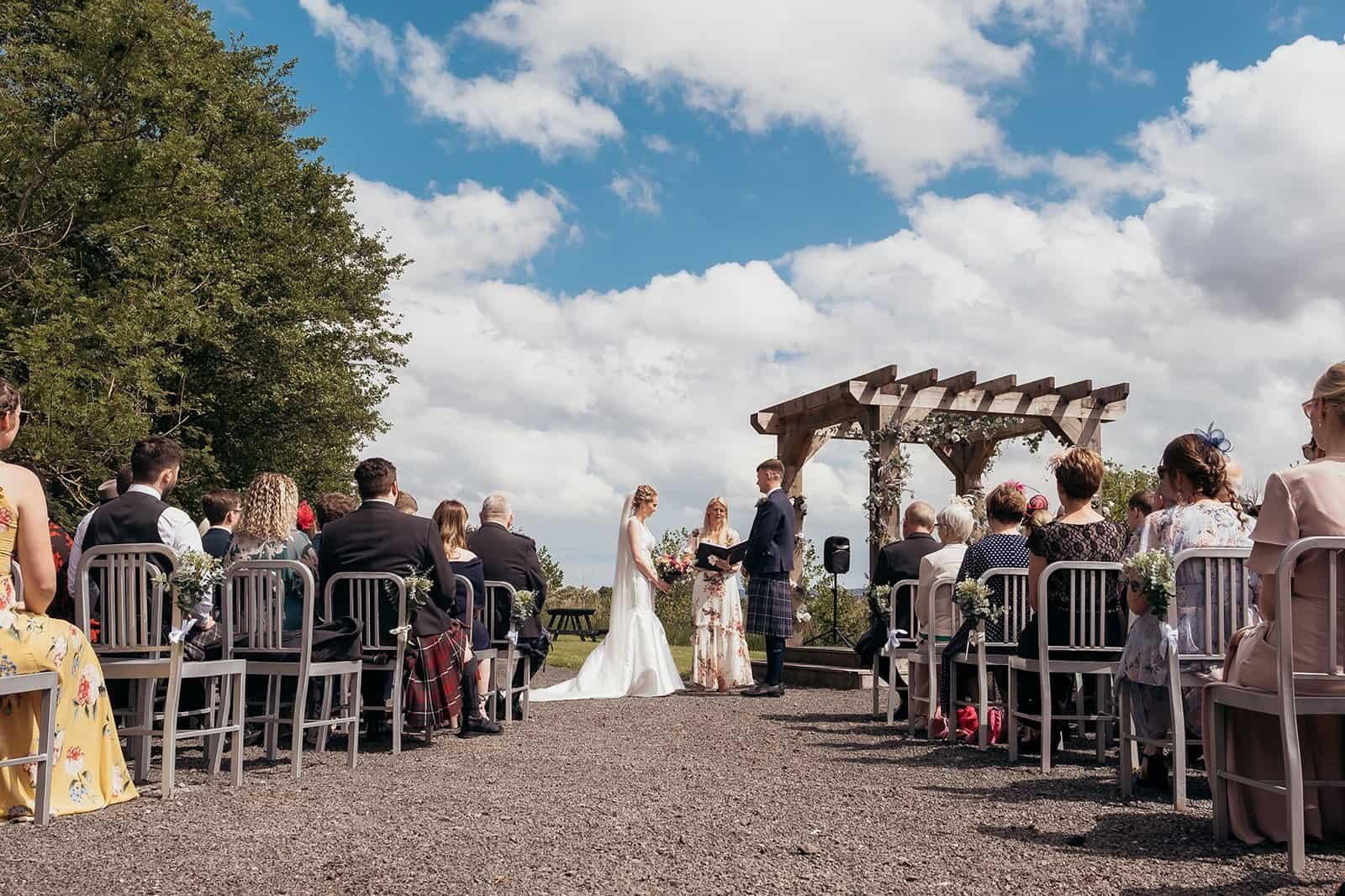 Outdoor wedding ceremony under clear sky with seated guests