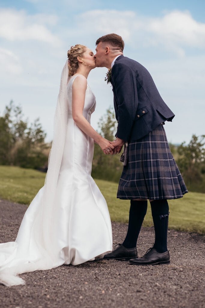 Bride and groom share a romantic kiss outdoors in wedding attire