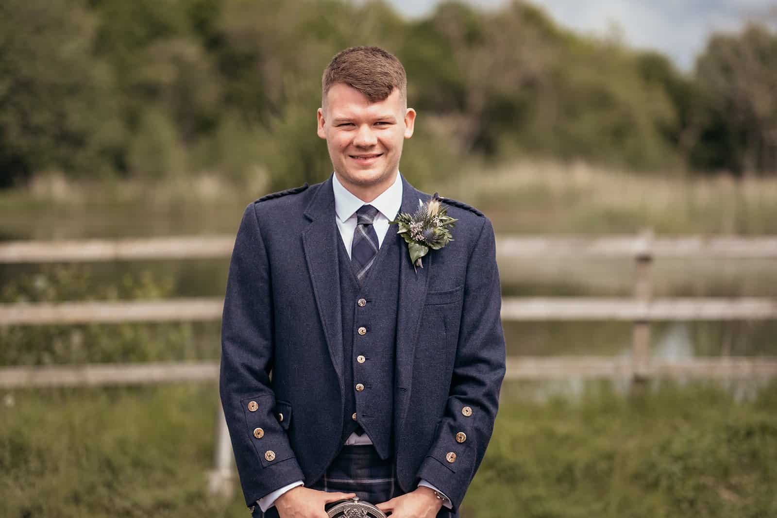 Man in blue suit standing outdoors with a wooden fence background