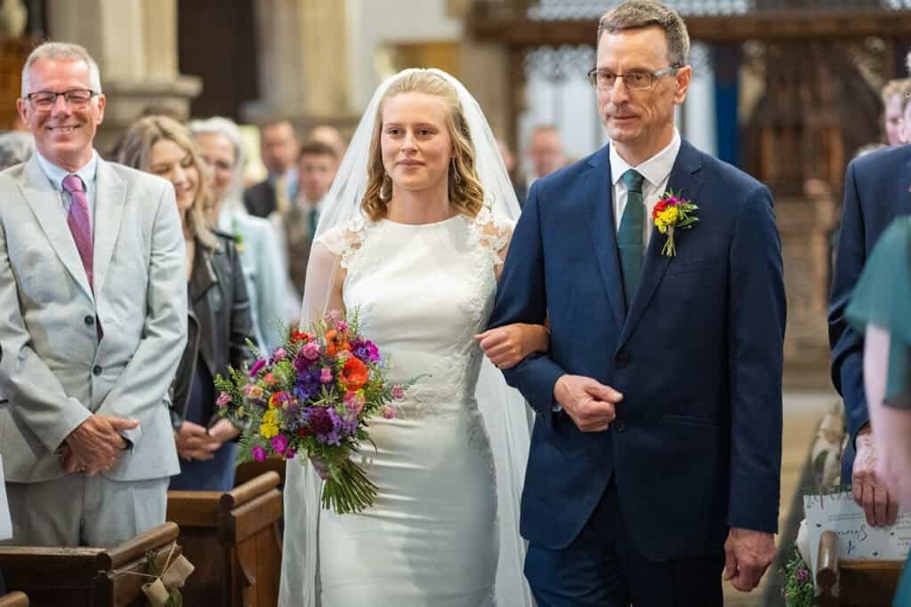 Bride walking down the aisle with her father with bouquet at a wedding ceremony at a church in Rothbury, Northumberland.
