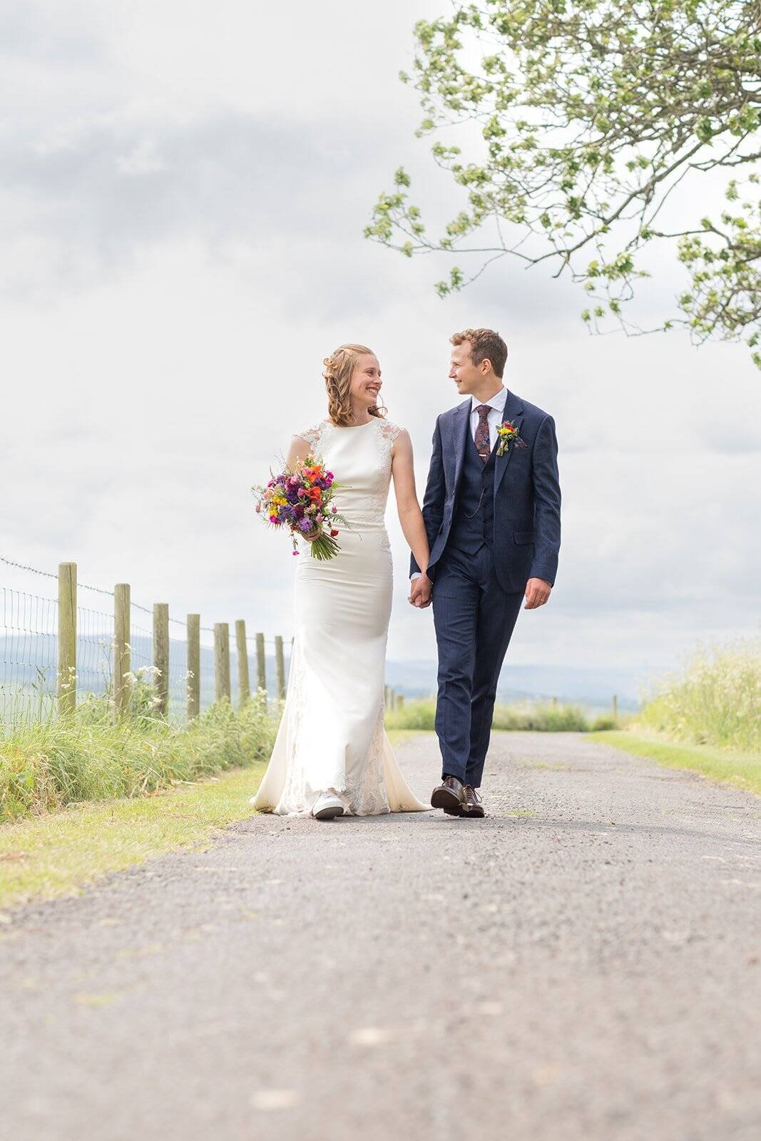 Bride and groom walking on scenic country road in wedding attire in Northumberland