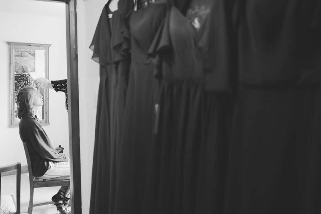 Bridal hair styling next to hanging bridesmaid dresses