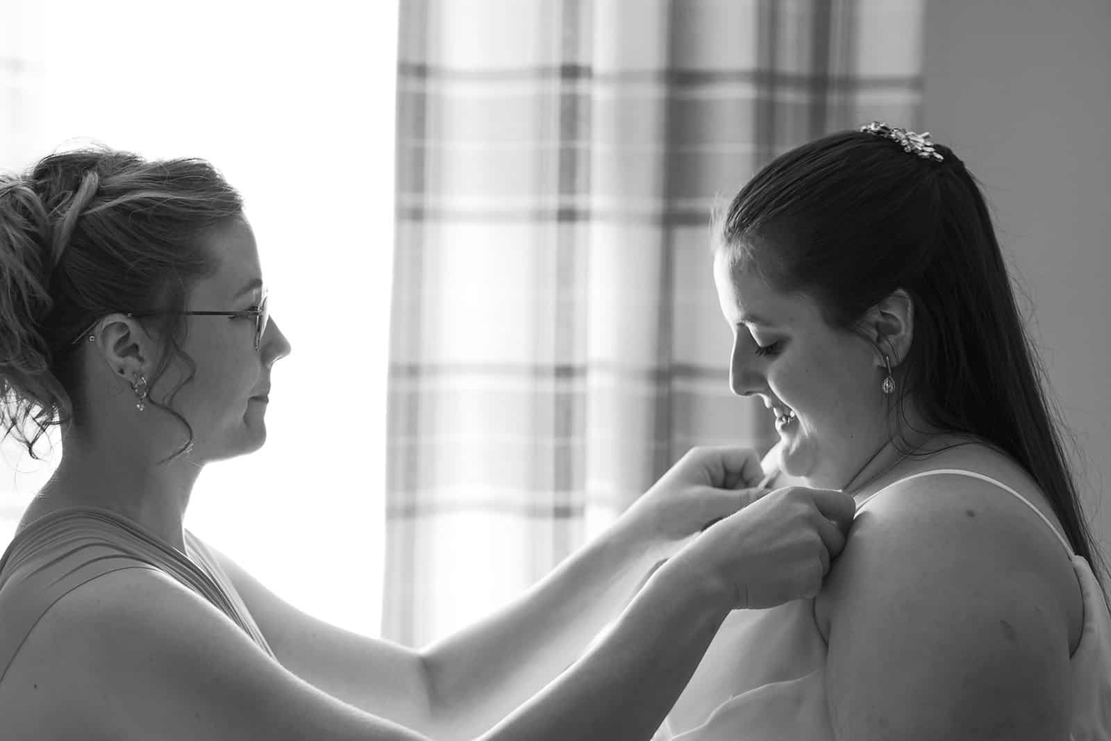 Woman helping another with wedding dress preparations