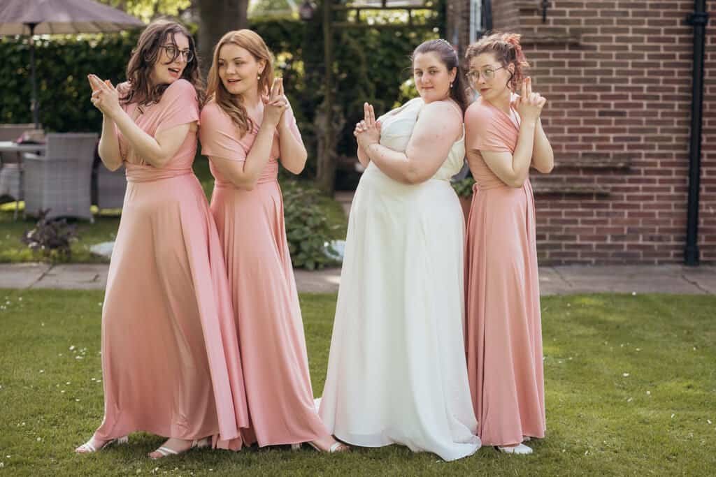 Bridesmaids in pink and bride posing playfully in a garden