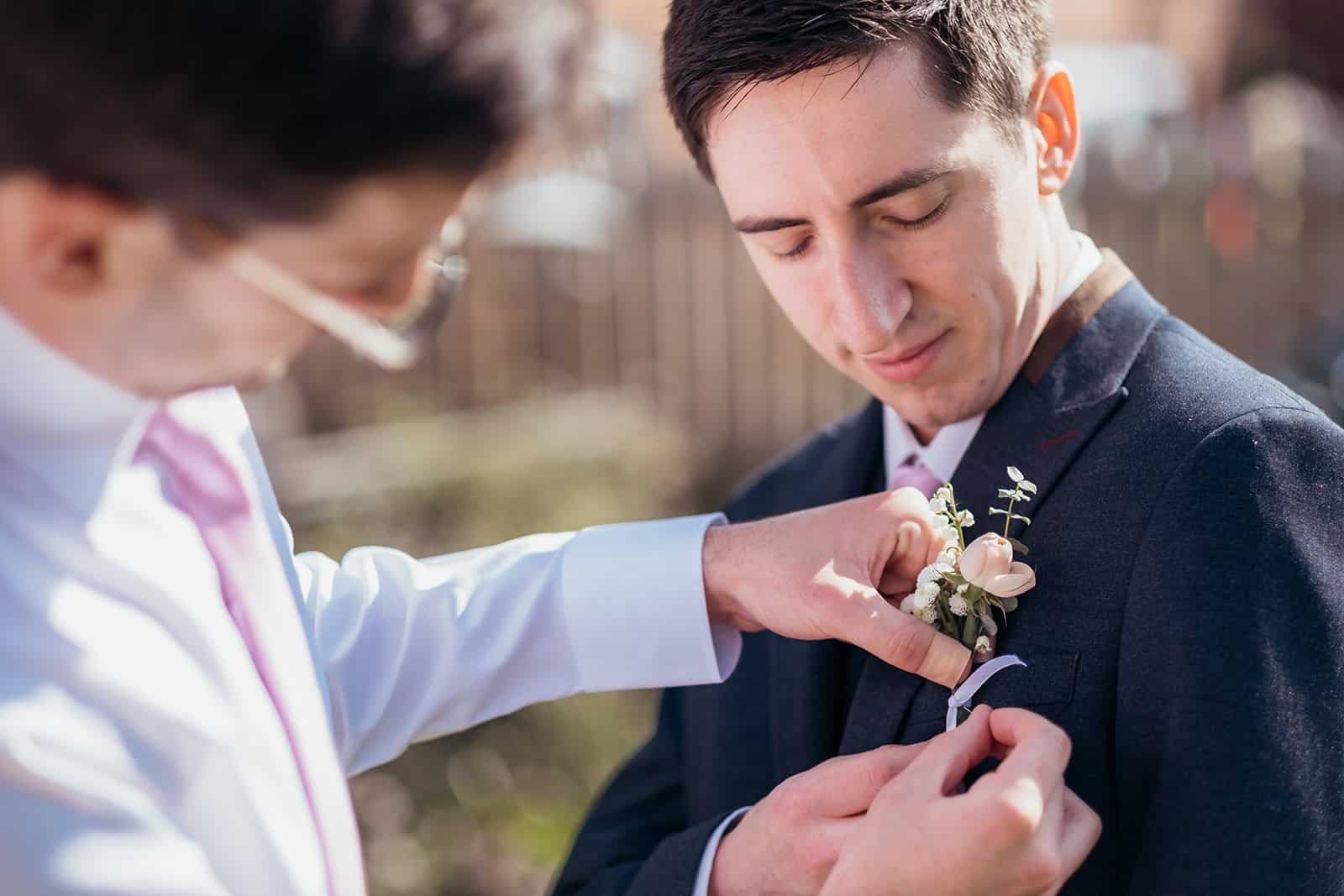 Groom adjusting boutonniere with the help of a groomsman