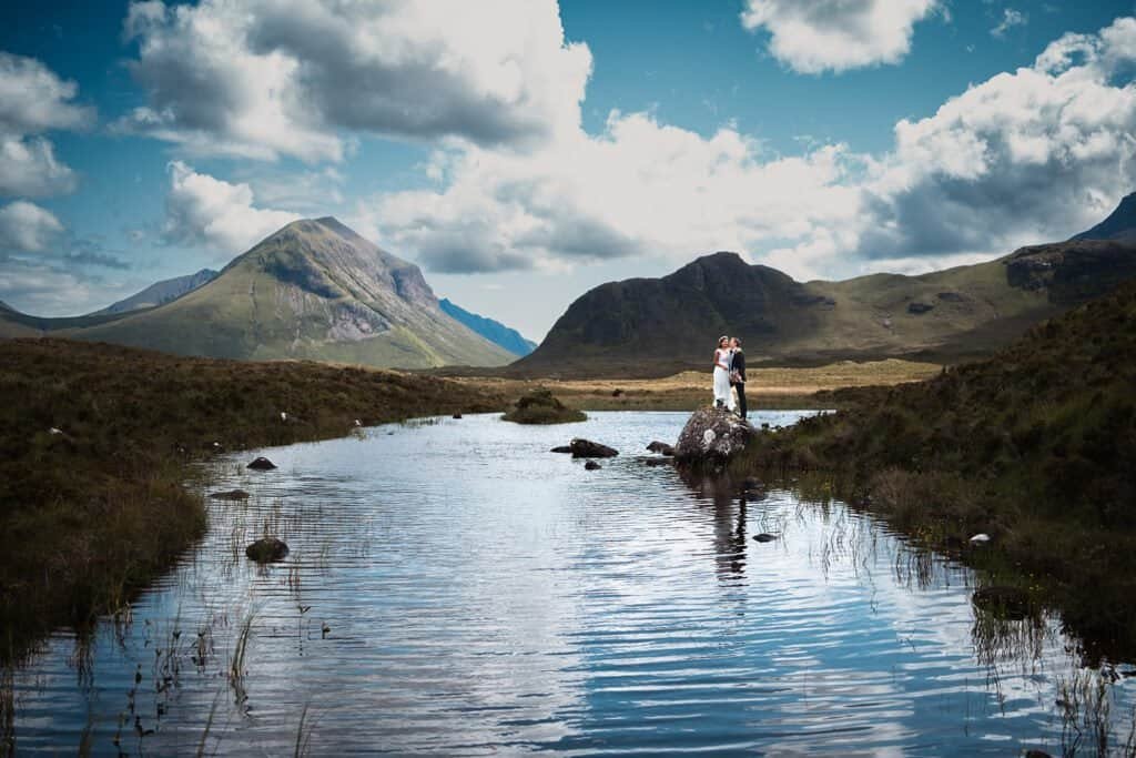 Bride and groom stand in serene mountain landscape by water on Isle of Skye