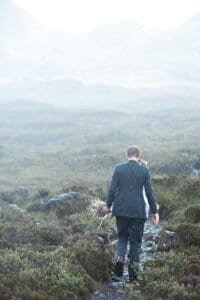 Groom walking through misty landscape with bouquet in hand