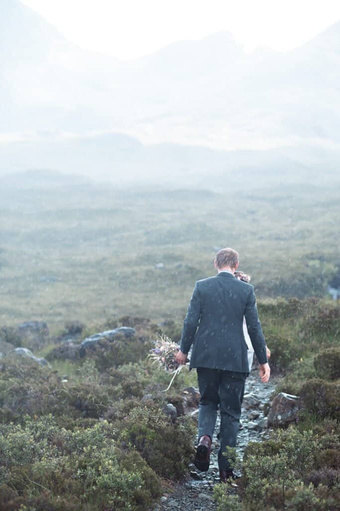 Groom walking through misty landscape with bouquet in hand