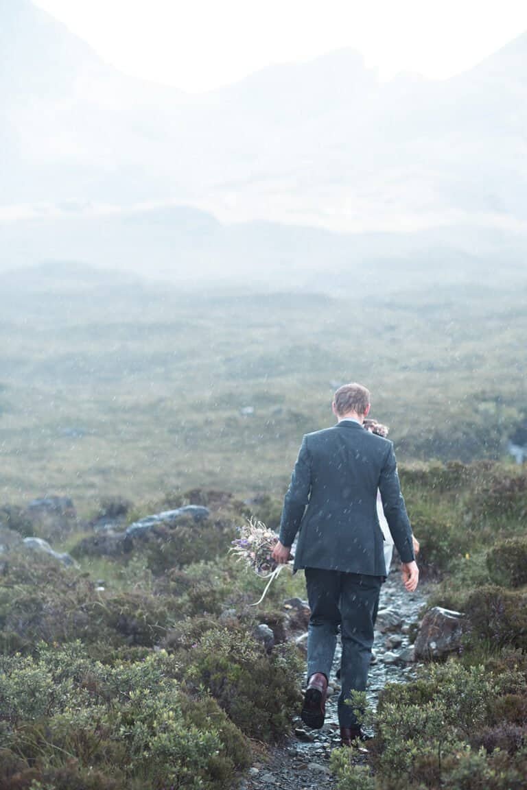 Groom walking through misty landscape with bouquet in hand