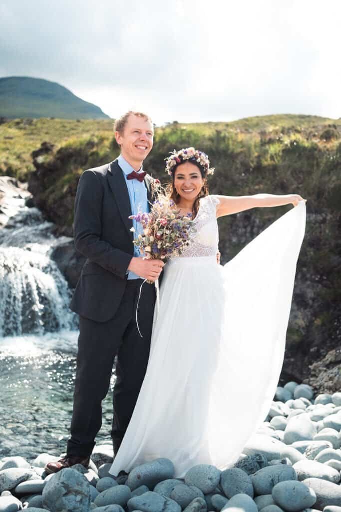 Smiling couple in wedding attire by a scenic waterfall outdoors