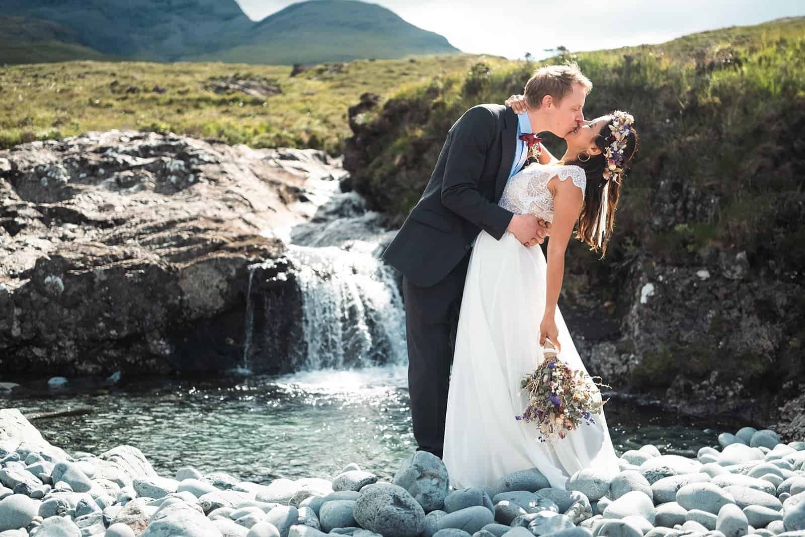 Bride and groom kissing by a mountain waterfall landscape