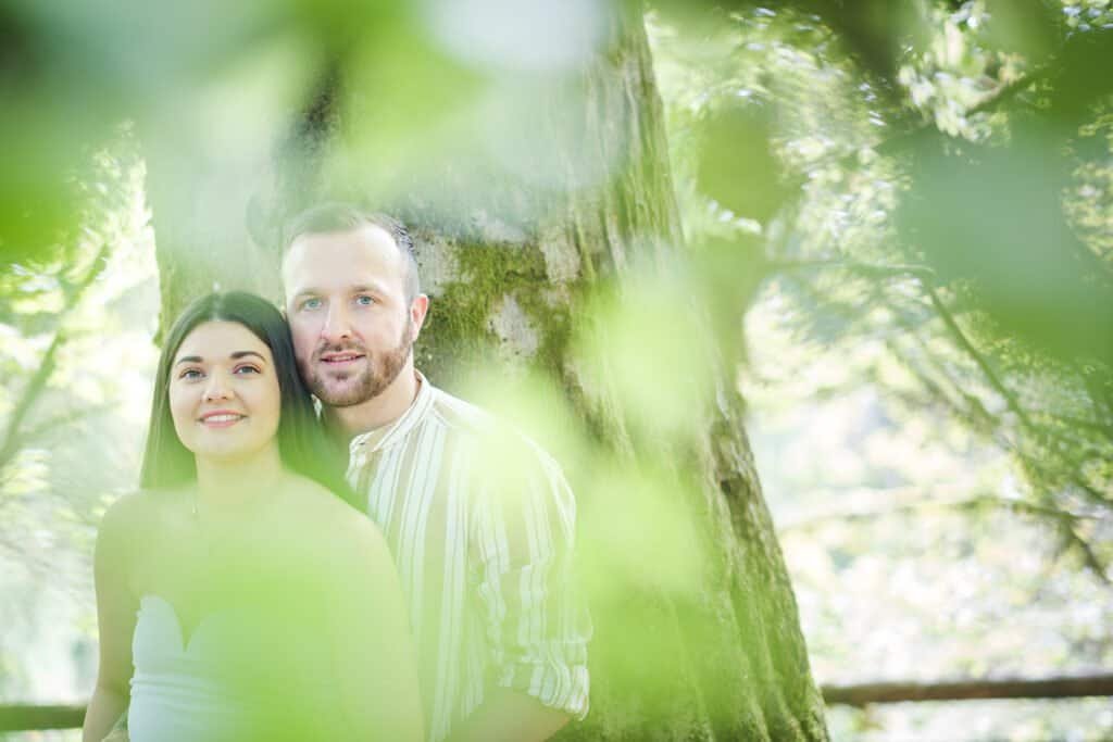 Smiling couple standing by a tree in a serene forest setting