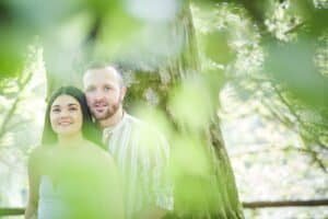 Smiling couple standing by a tree in a serene forest setting