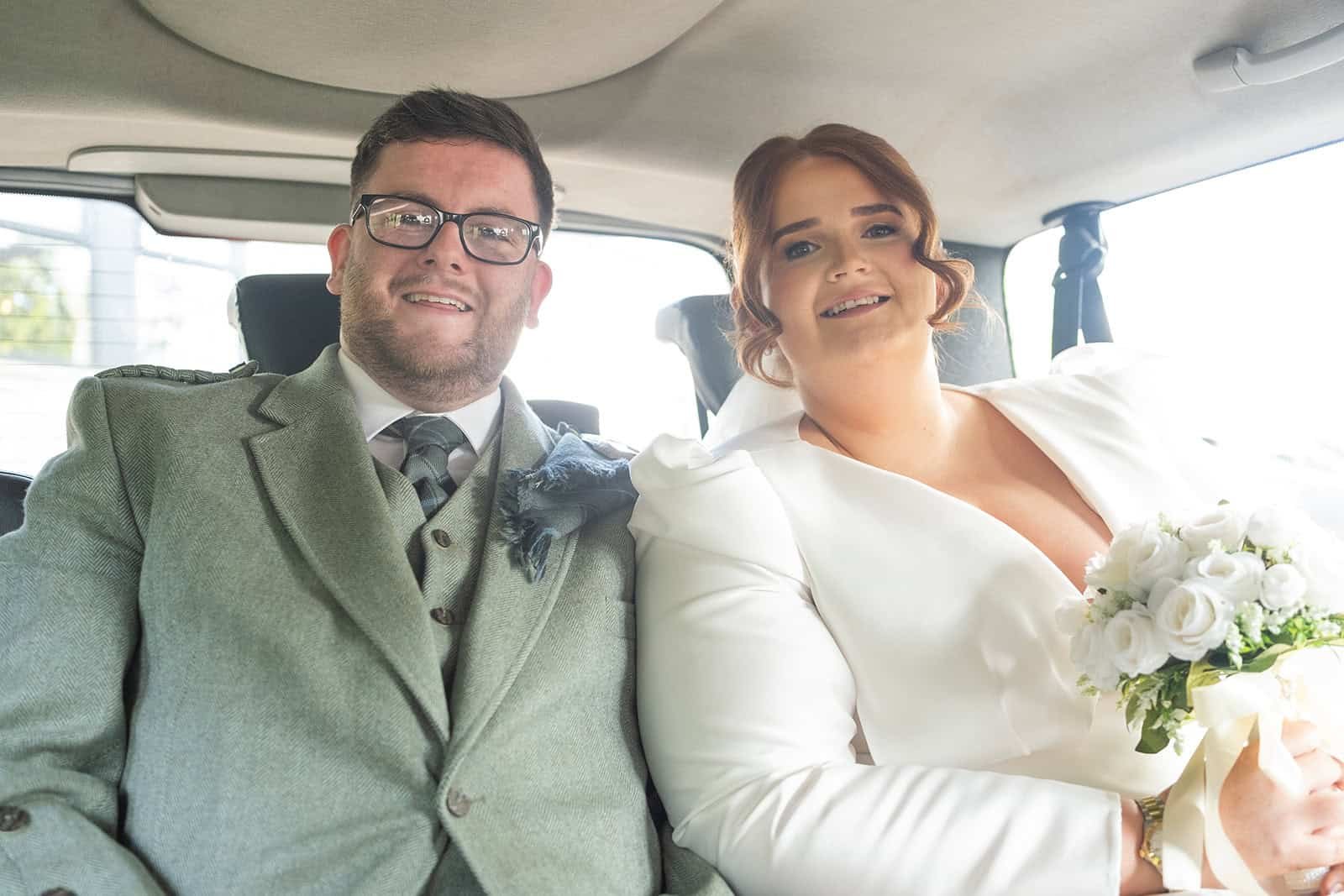 Happy wedding couple smiling inside a car with a bouquet