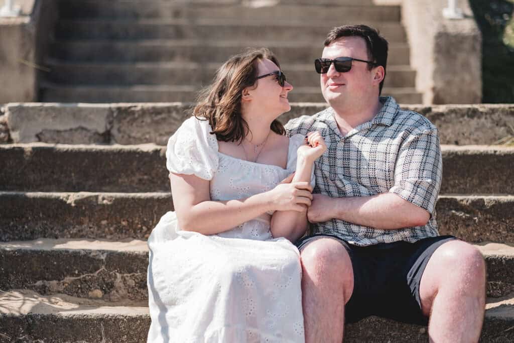 A smiling couple sitting on stone steps in summertime at Seaburn