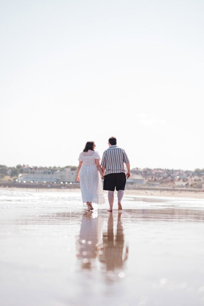 Couple holding hands walking on a sunny beach in summer