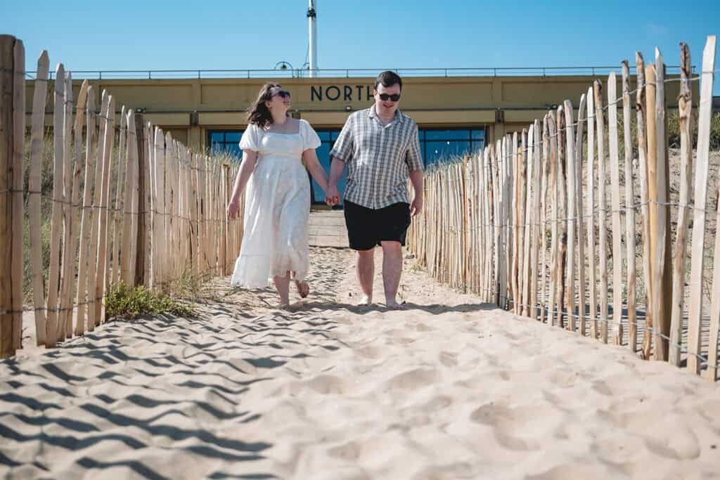 Couple walking on sandy beach path beneath clear blue sky