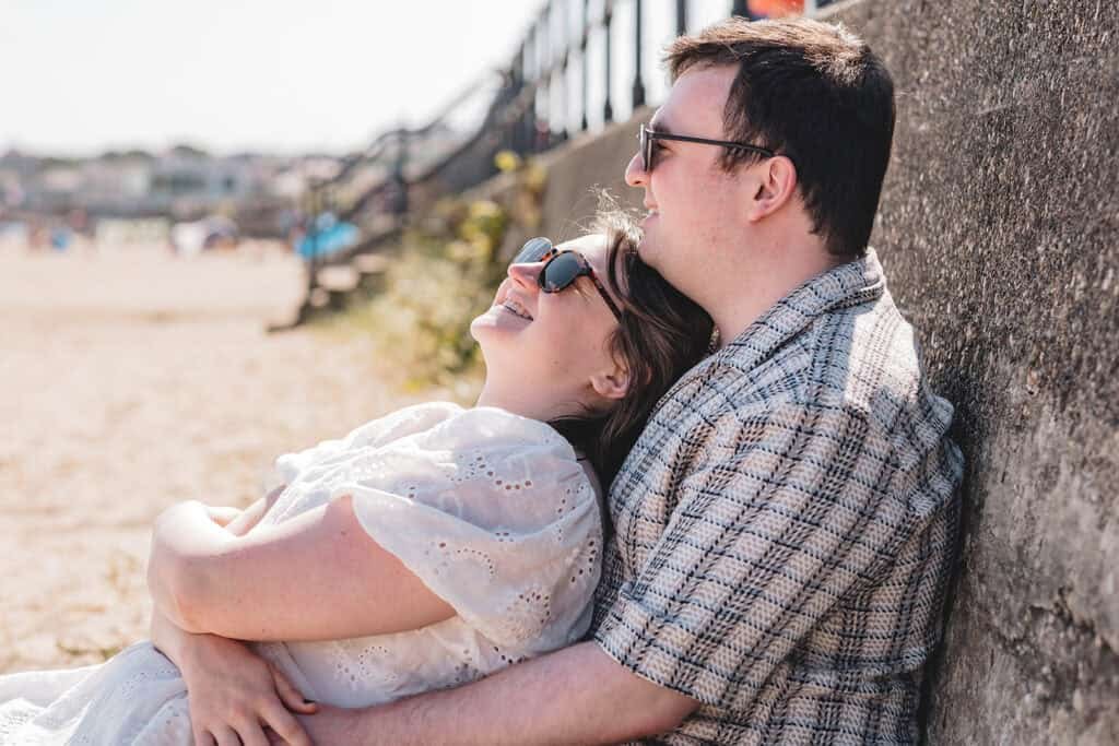 Couple relaxing on beach against a stone wall in sunlight