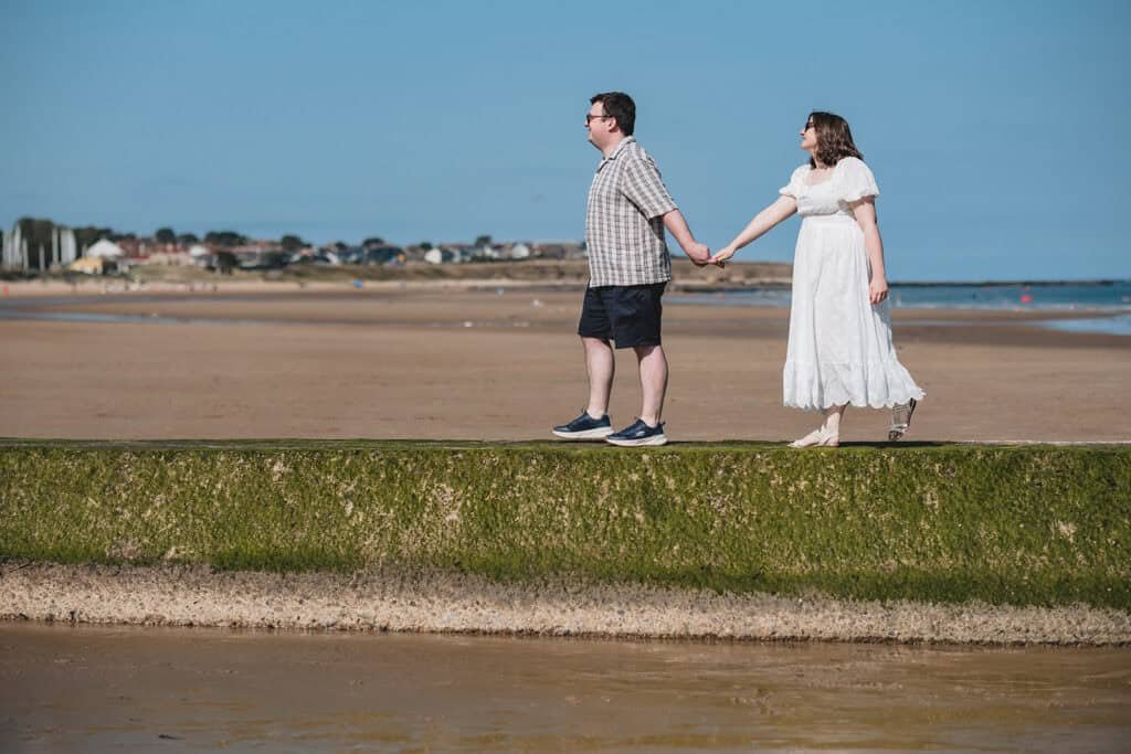 Couple holding hands walking on the beach under blue sky