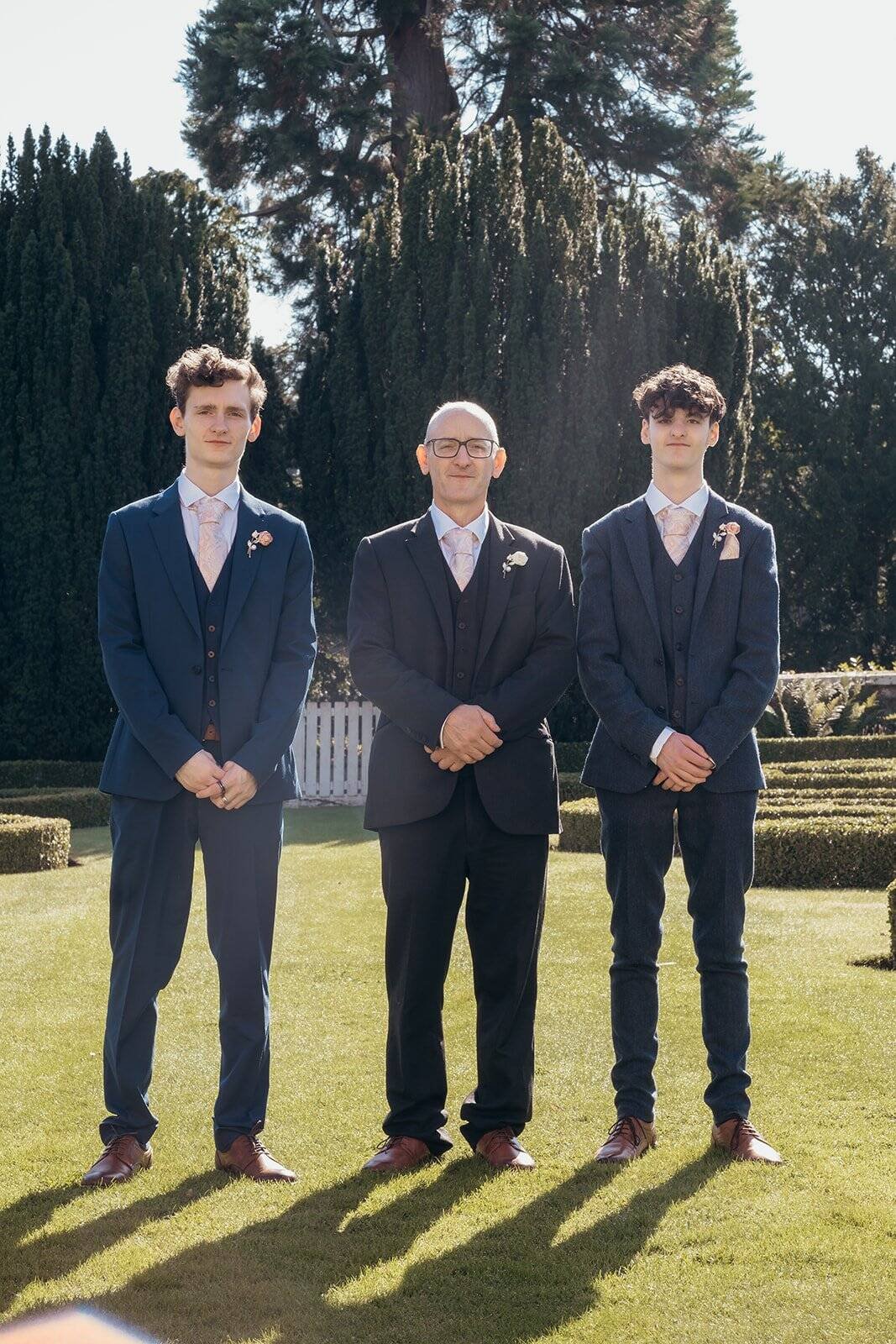 Three men in suits standing in a beautiful garden setting