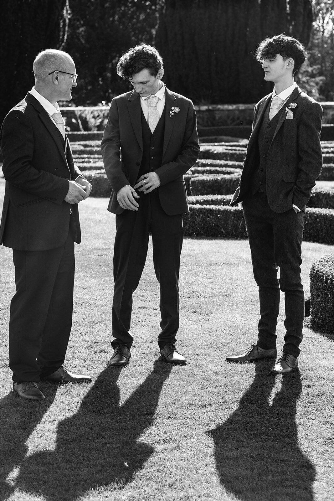 Three men in formal suits standing in a garden setting