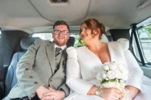 Bride and groom smiling in a car on their wedding day