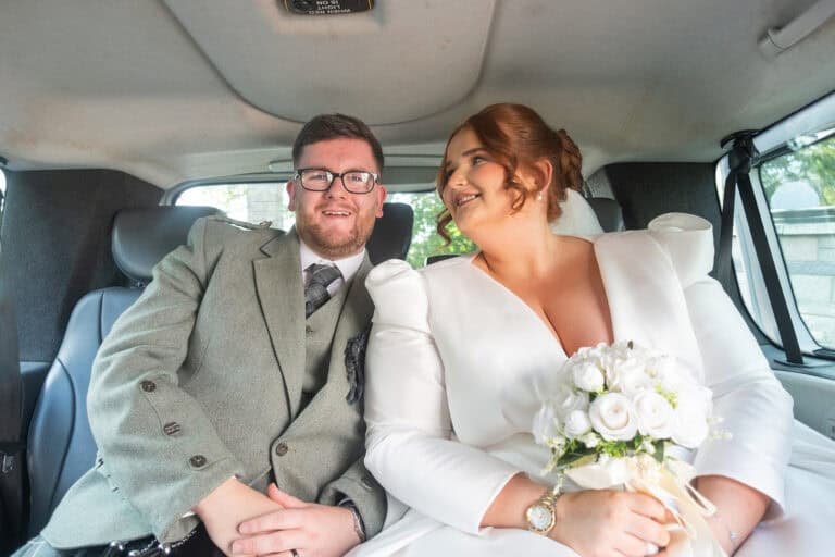 Bride and groom smiling in a car on their wedding day