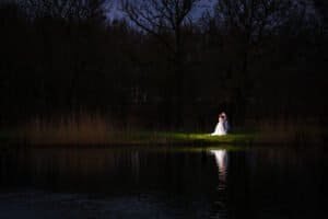 Bride and groom illuminated by moonlight near a serene lake