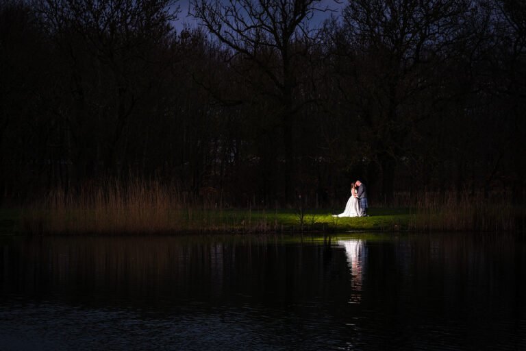 Bride and groom illuminated by moonlight near a serene lake