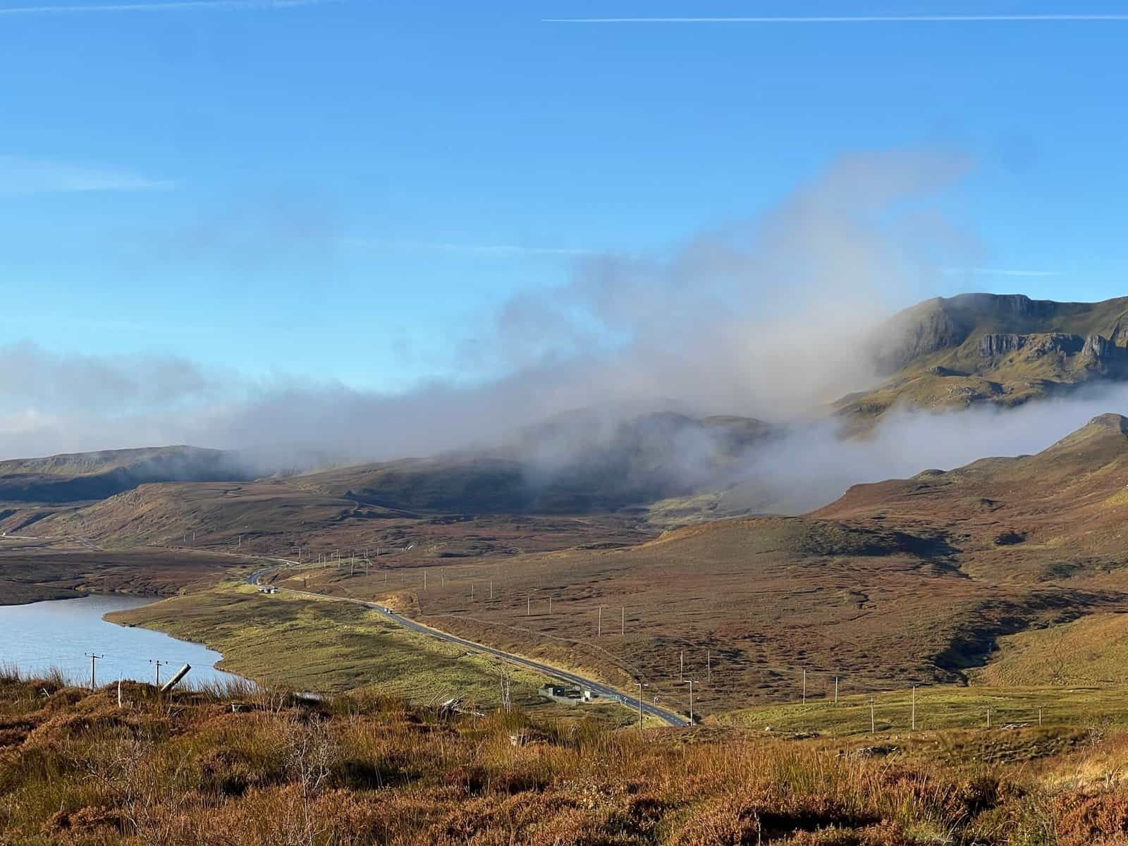 Mist lifting over the hills and a winding road beside a loch on the Isle of Skye