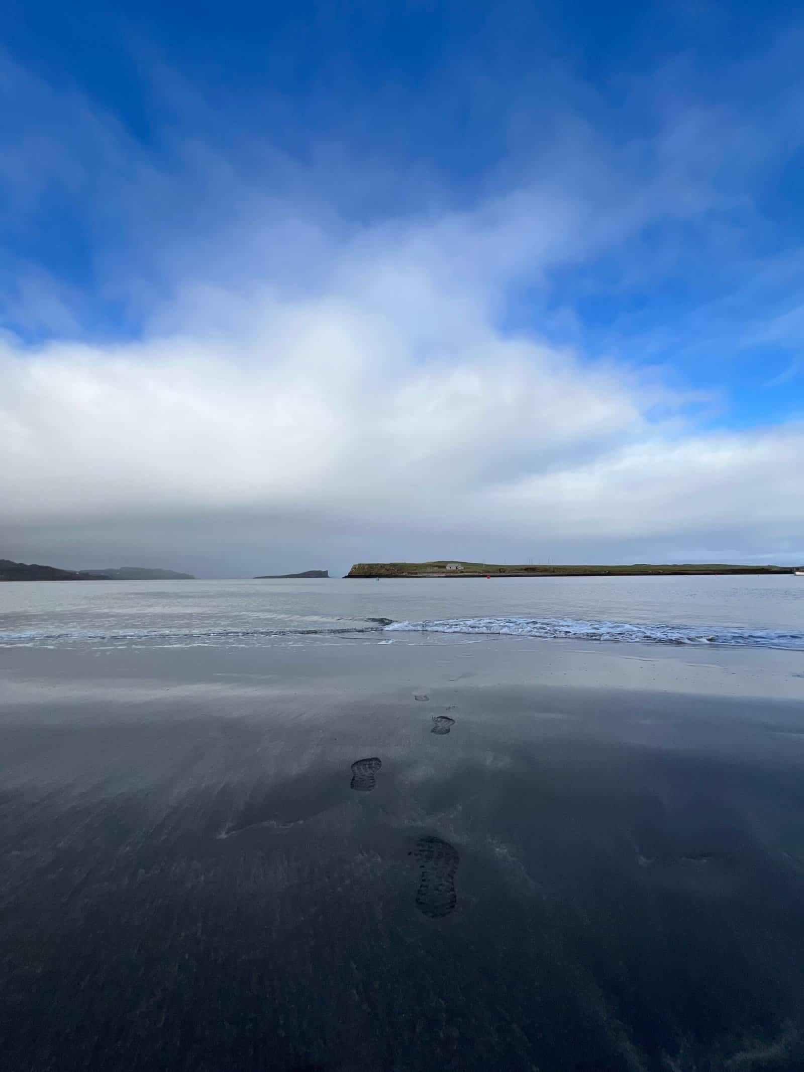 Footprints on black sand beach with cloudy sky above