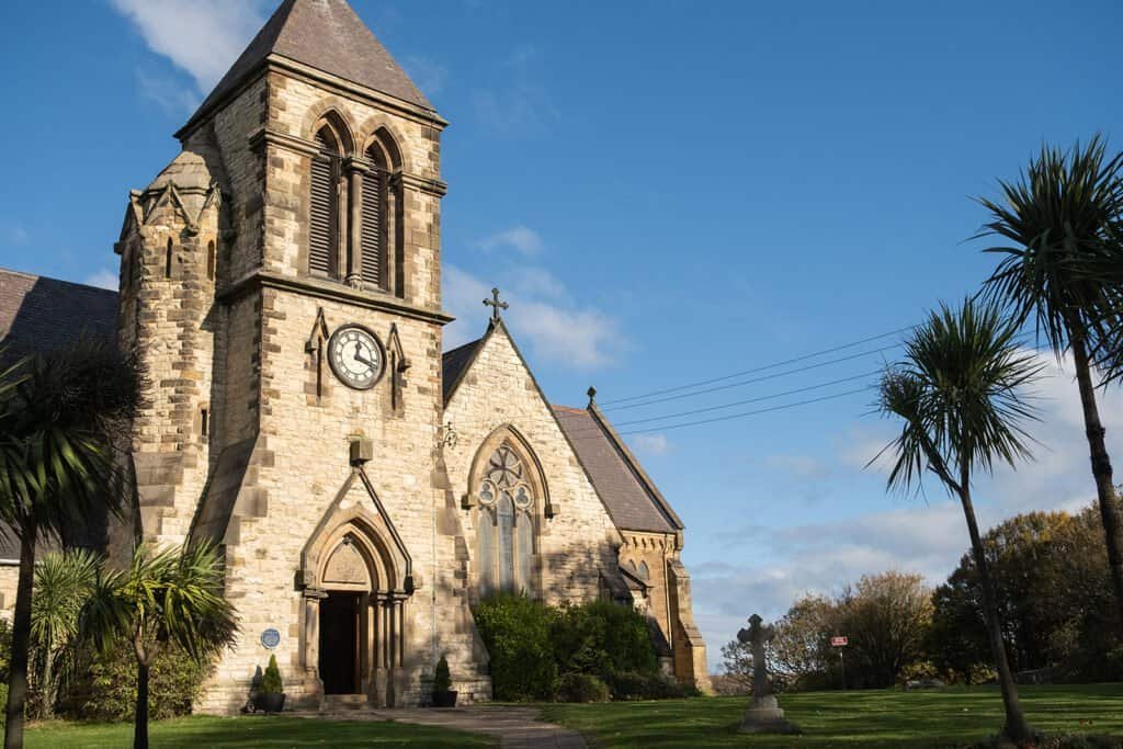 Stone church with clock tower surrounded by green trees and grass