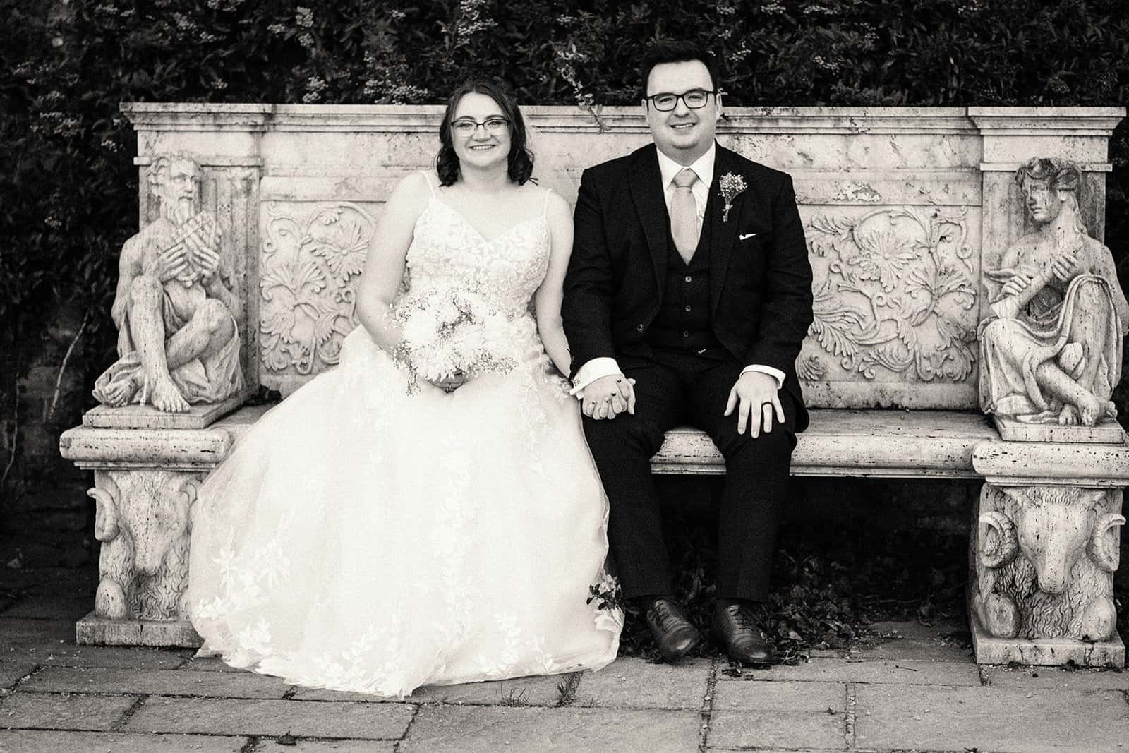 Bride and groom sitting on ornate stone bench smiling together