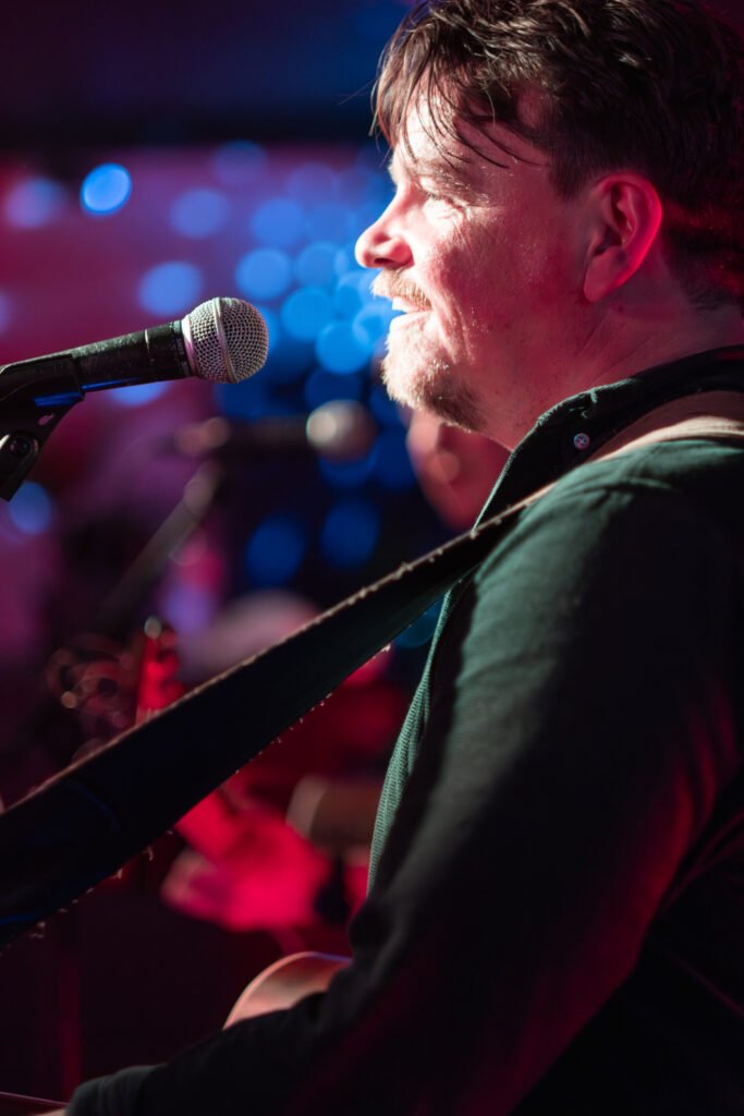 Singer performing live on stage with a guitar in the spotlight