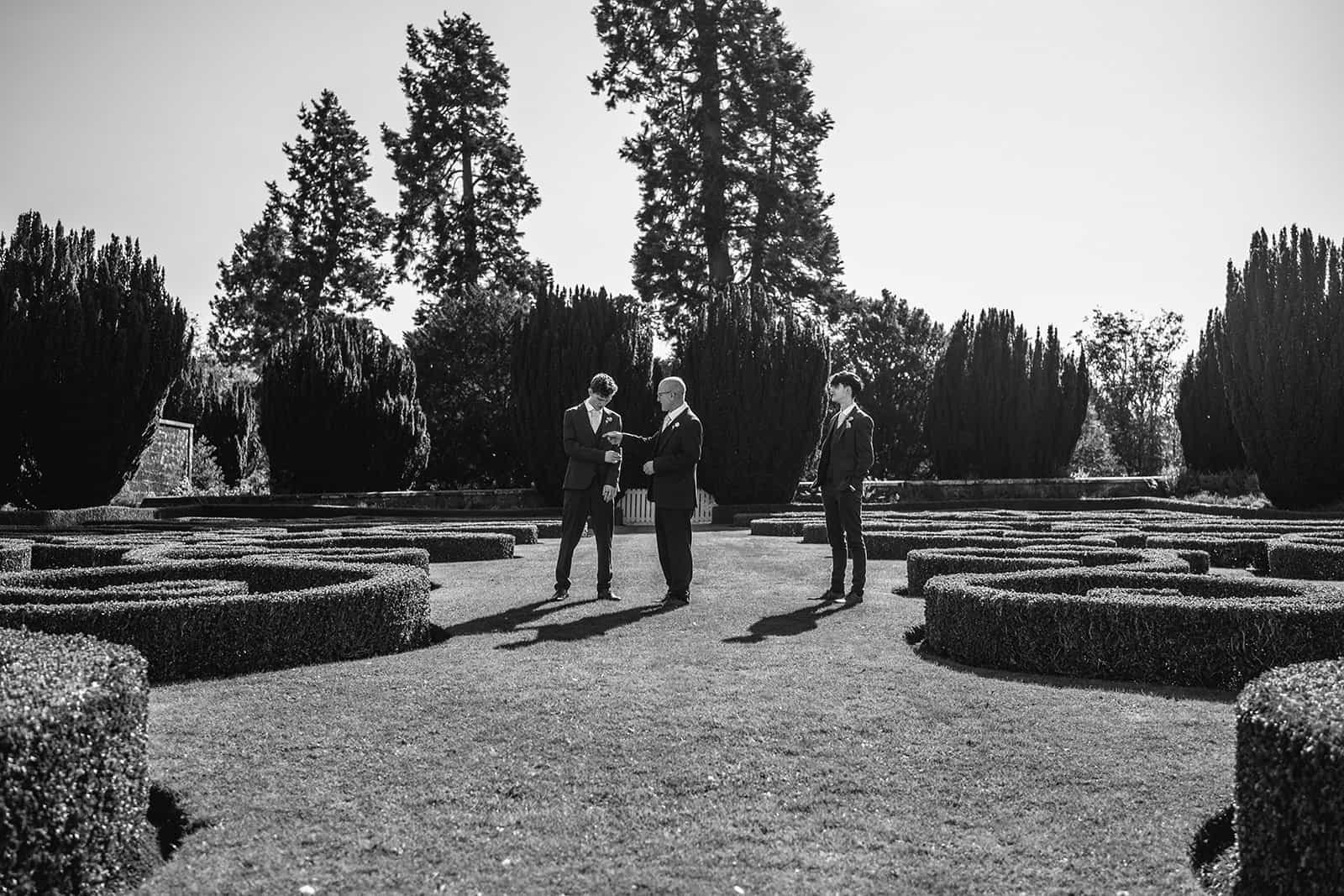 Three people standing in formal attire in a garden setting