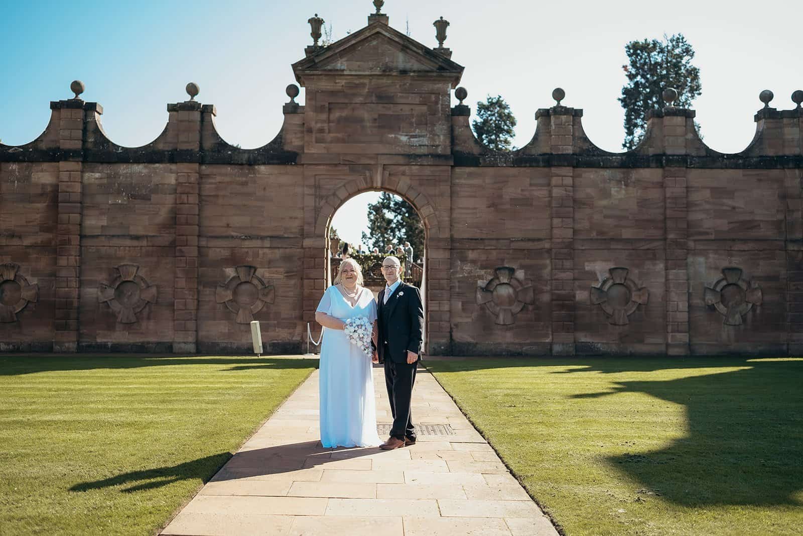 Couple posing in front of historic stone archway on sunny day