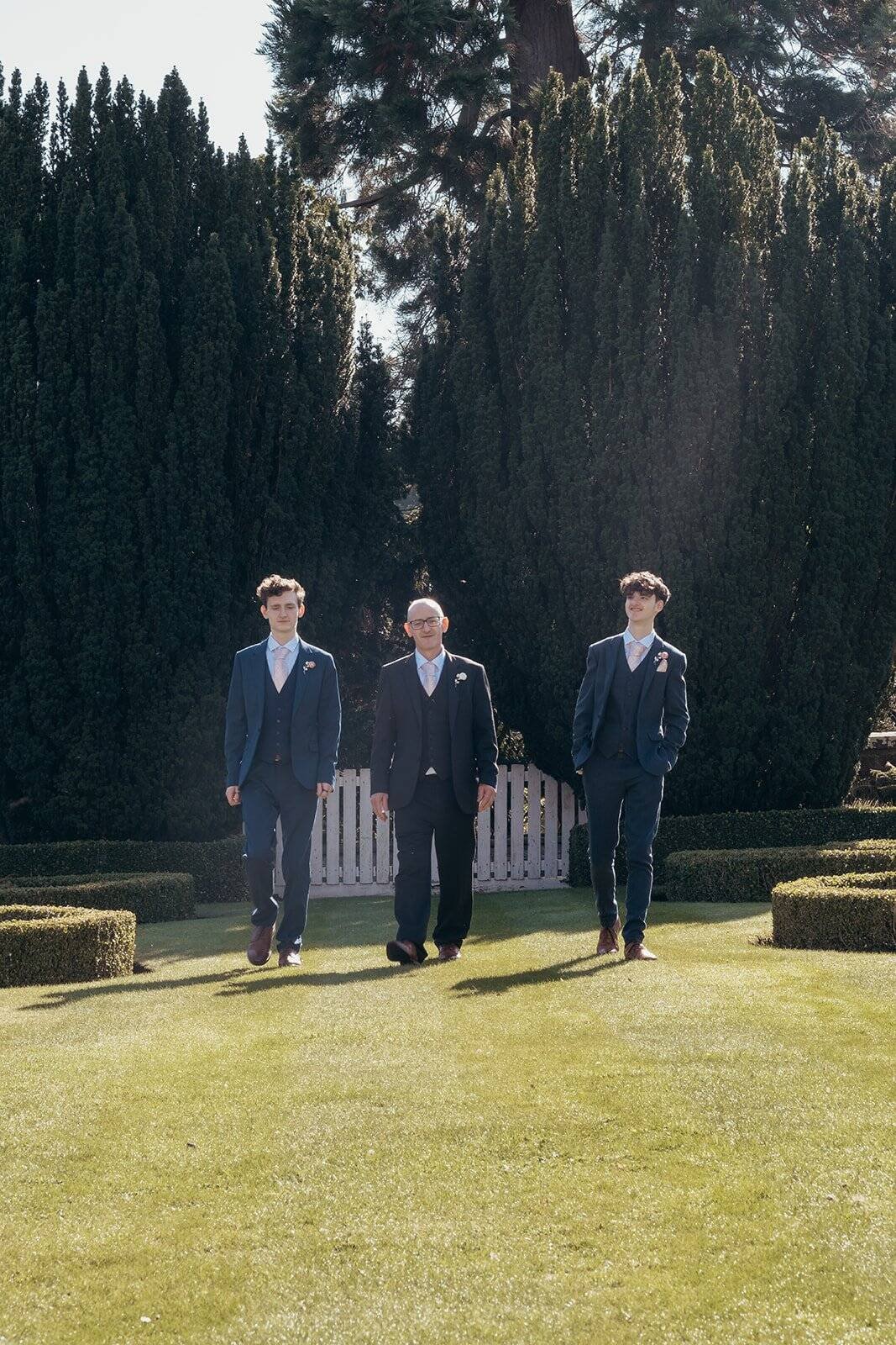 Three men in suits walking in the gardens at Chatelherault