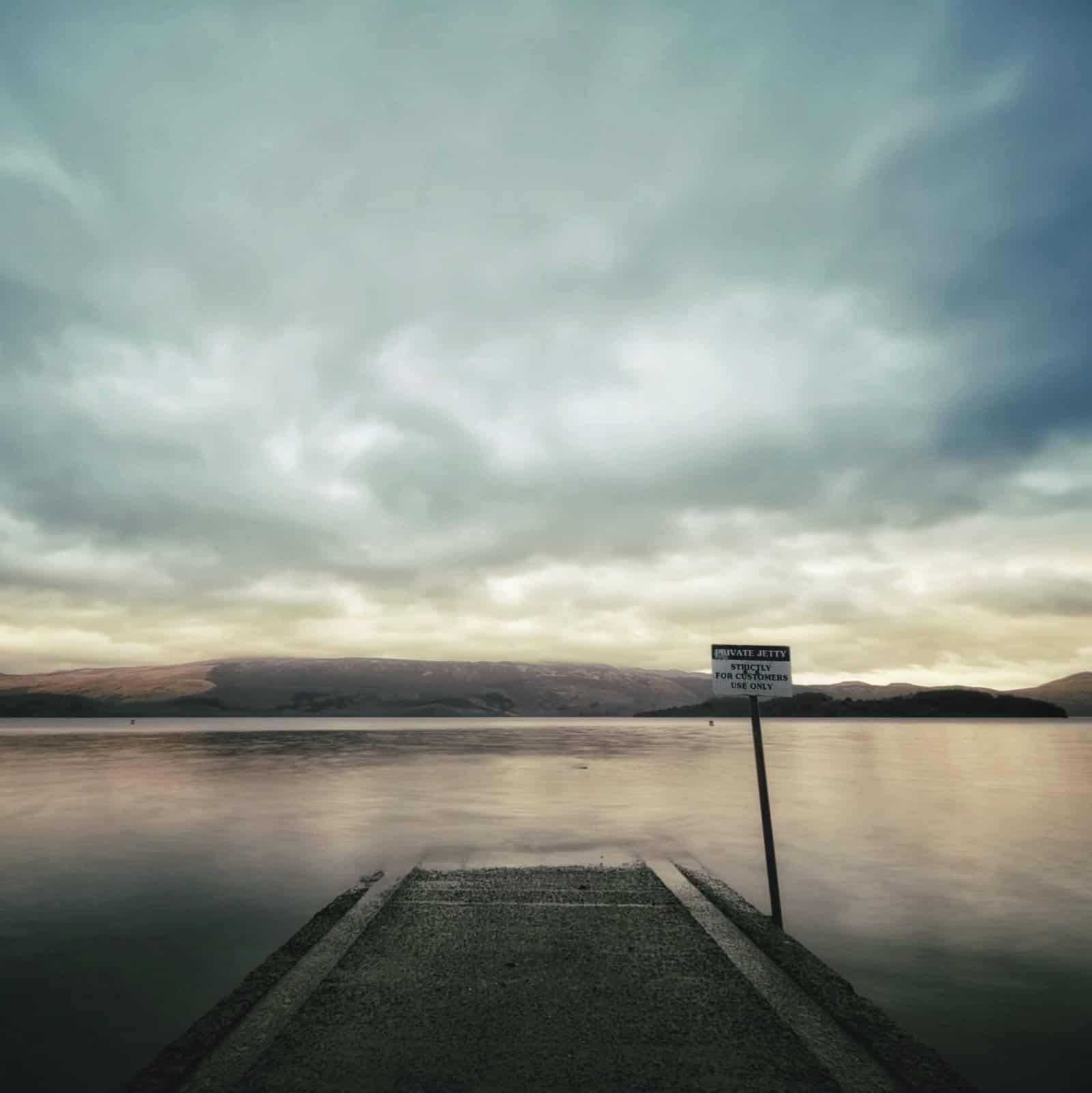 Serene lake view with cloudy sky and a wooden pier at dawn