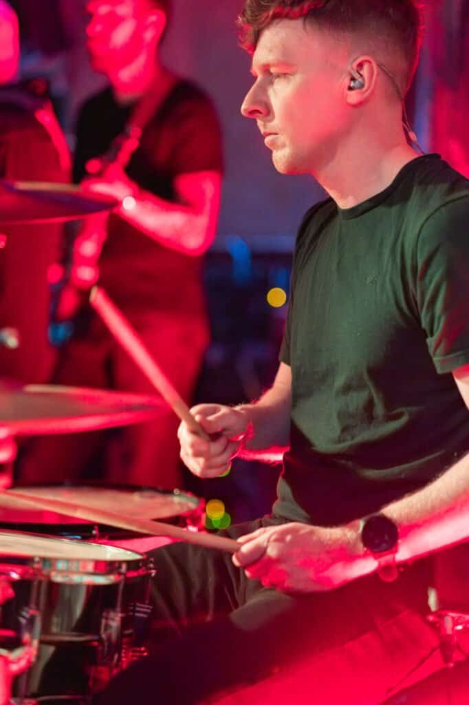 Drummer playing energetically on stage with red lighting